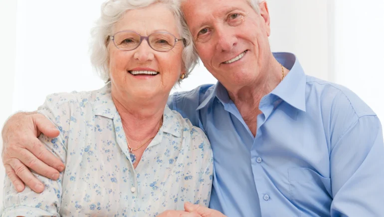 Photo of a senior couple seated, the man hugging the woman's shoulders (upper body shot)